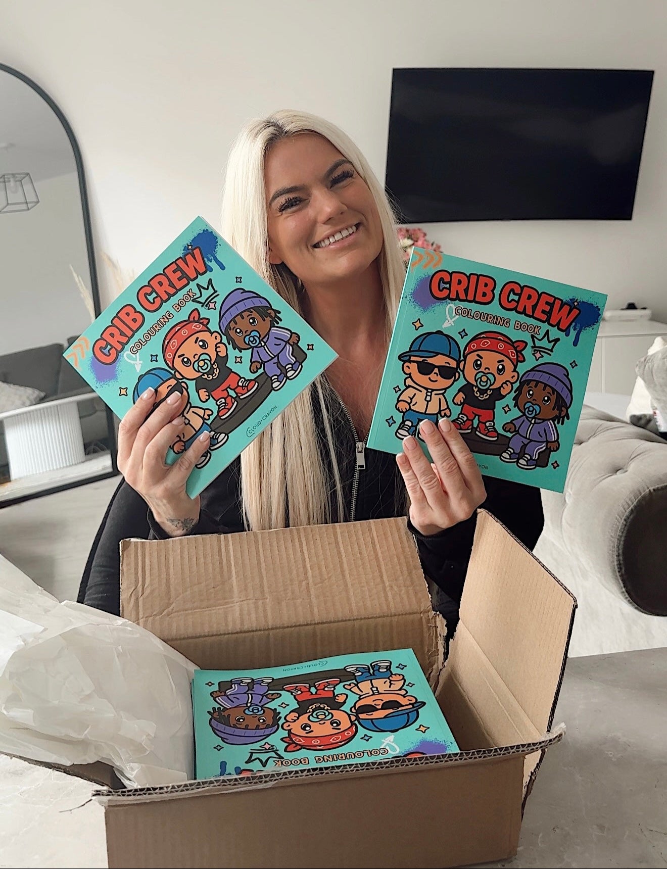 Owner of Cloud and Crayon holding 'Crib Crew' colouring book in a box with a neutral background